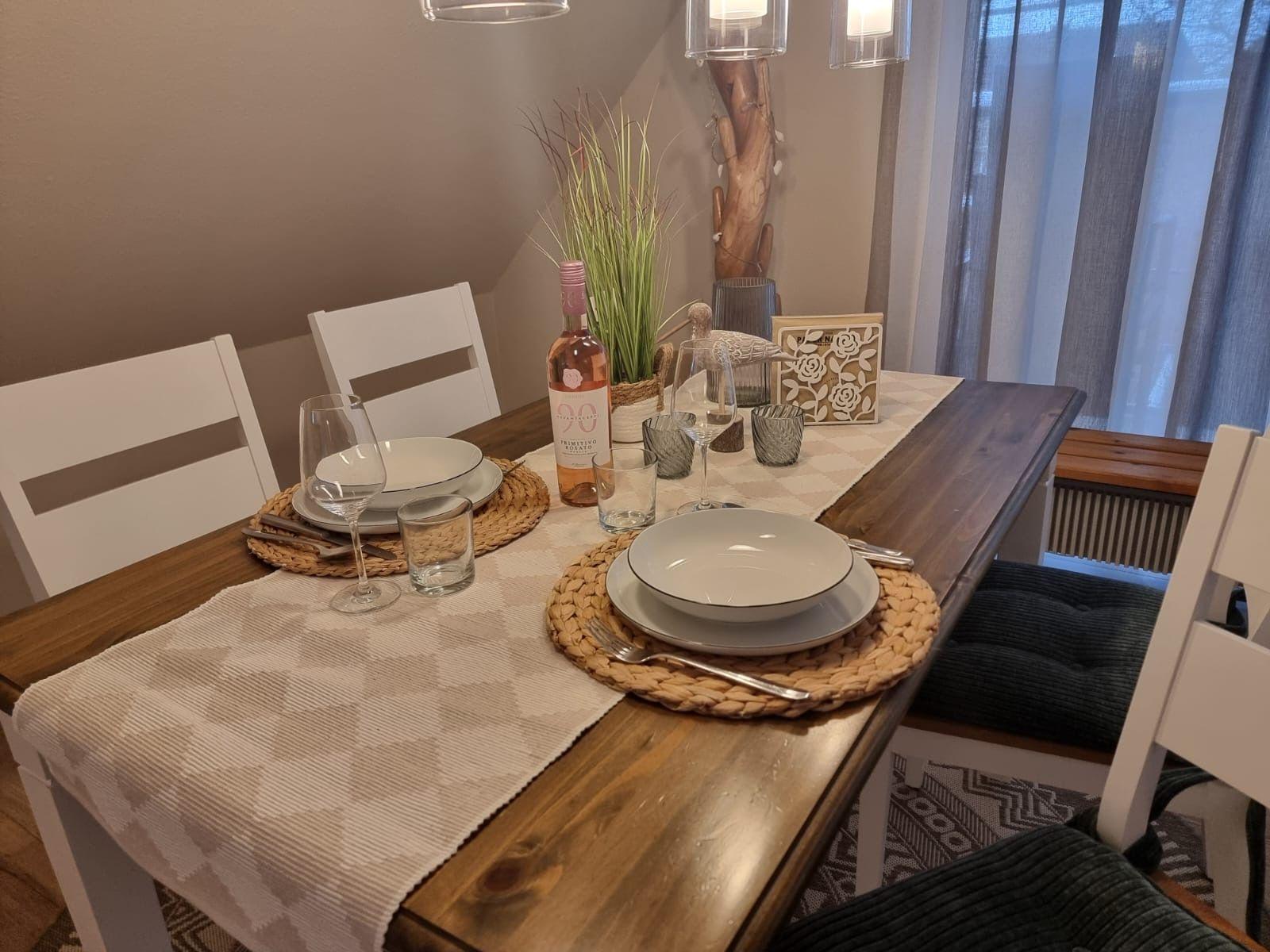 Dining table set for four with a bottle of red wine.