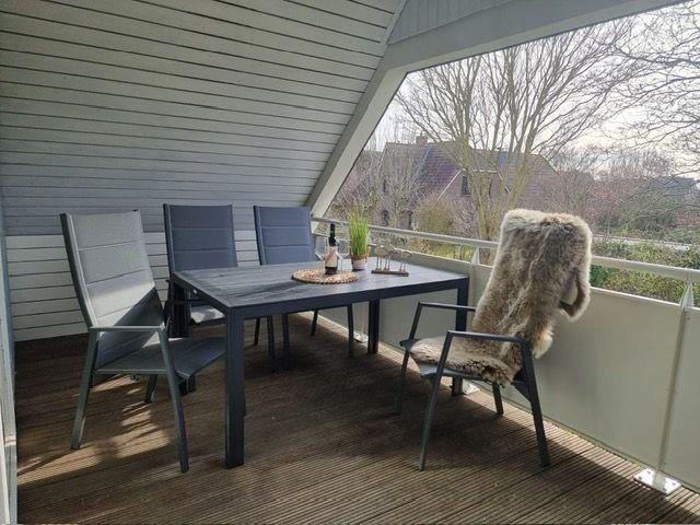 Terrace with table, four chairs, and fur blanket. View of trees and houses.