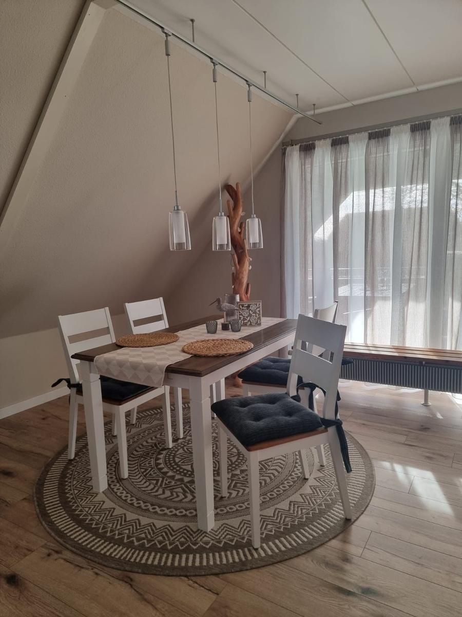 Dining area with table, chairs, and pendant lights. Round rug and window with curtains.