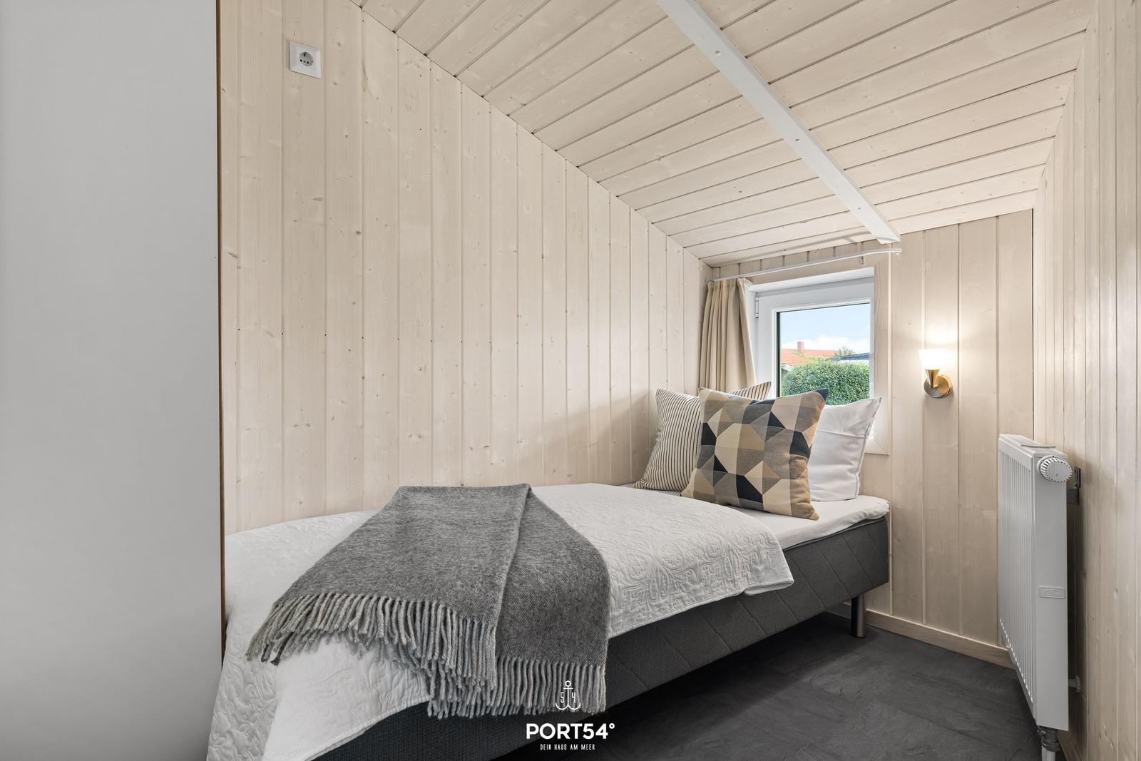 Schlafzimmer mit Bett, Fenster und Holzwandverkleidung.
