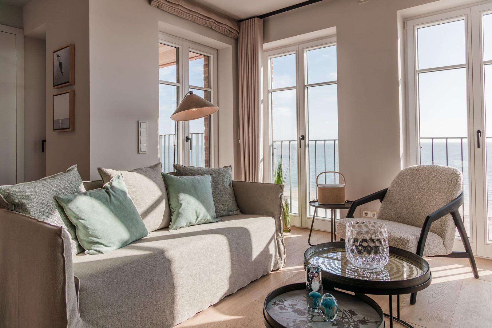Wohnzimmer mit Sofa, Sessel und Blick aufs Meer durch große Fenster.