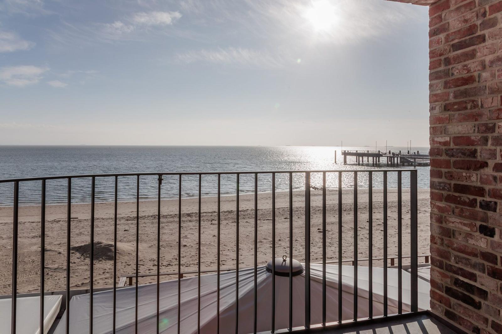 Blick von Balkon auf Strand und Meer mit Steg im Hintergrund.