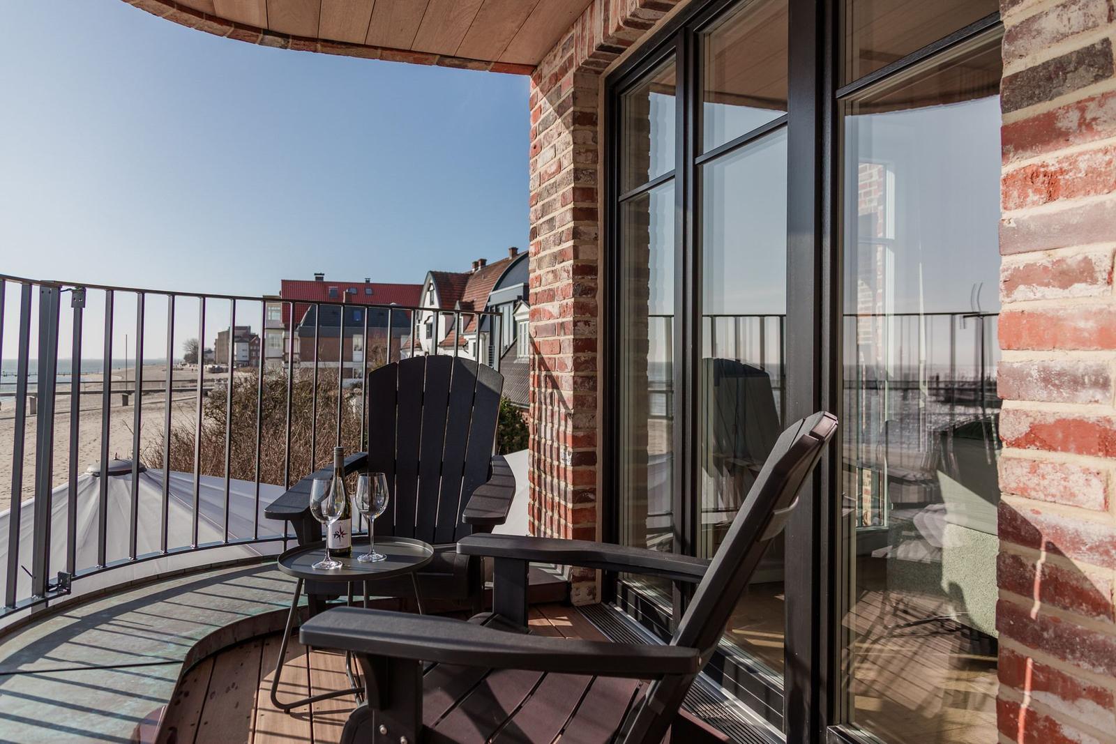 Terrasse mit Sitzgelegenheit und Meerblick. Roter Backstein und Glasfront.