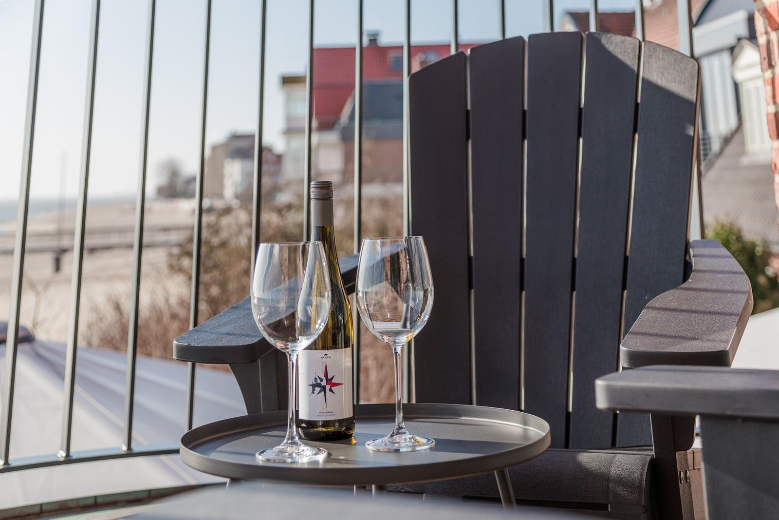 Auf der Terrasse steht ein Tisch mit zwei Gläsern und einer Weinflasche vor einem dunklen Stuhl.
