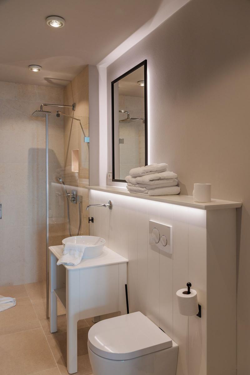 Badezimmer mit Dusche, Waschtisch und Toilette. Weiße Möbel und Handtücher.