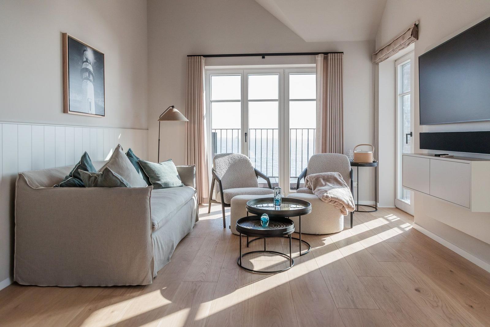 Wohnzimmer mit Sofa, Sesseln und TV. Balkon mit Blick auf Wasser.
