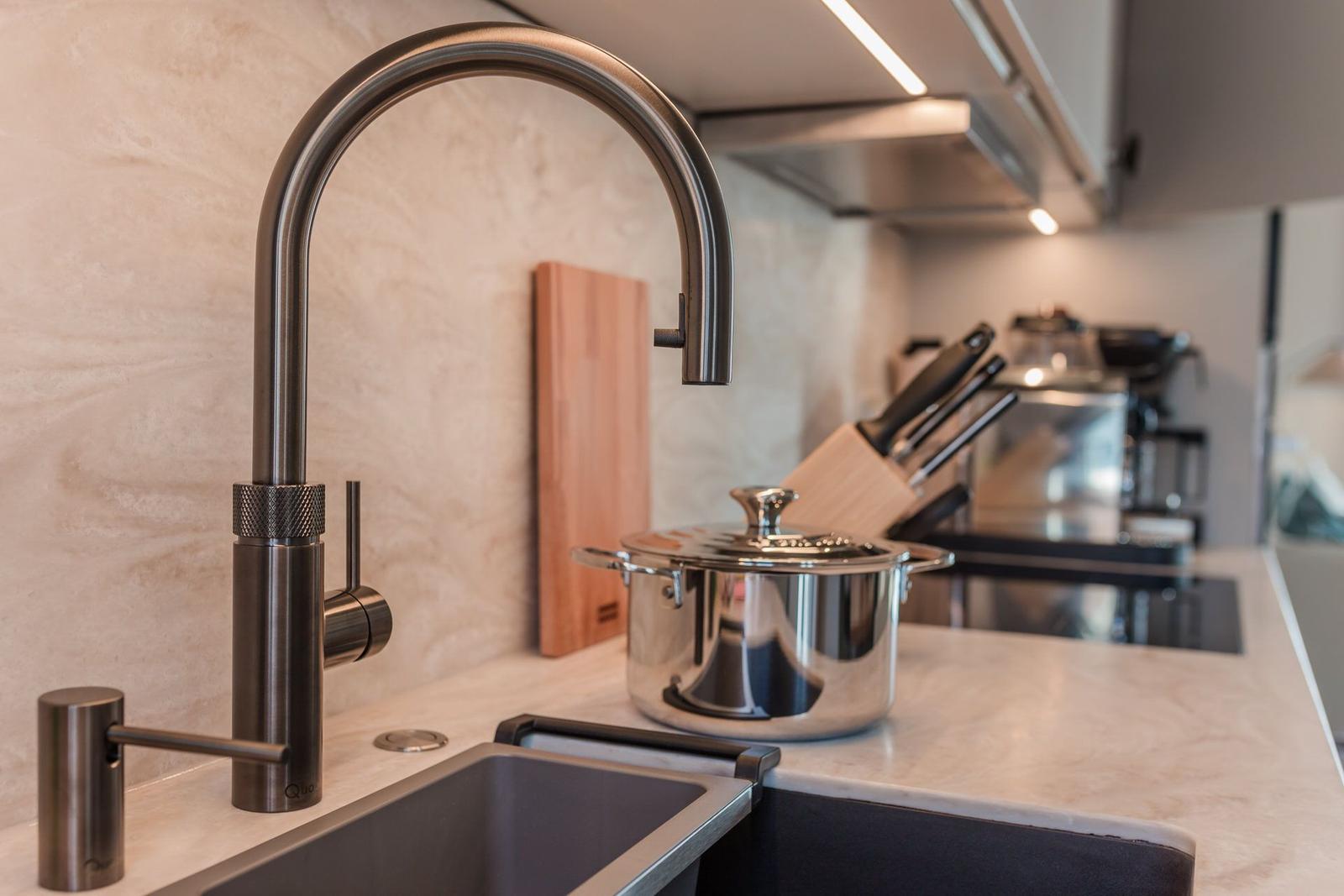 Moderne Küche mit Edelstahlspüle, Wasserhahn und Kochtopf auf Arbeitsfläche.