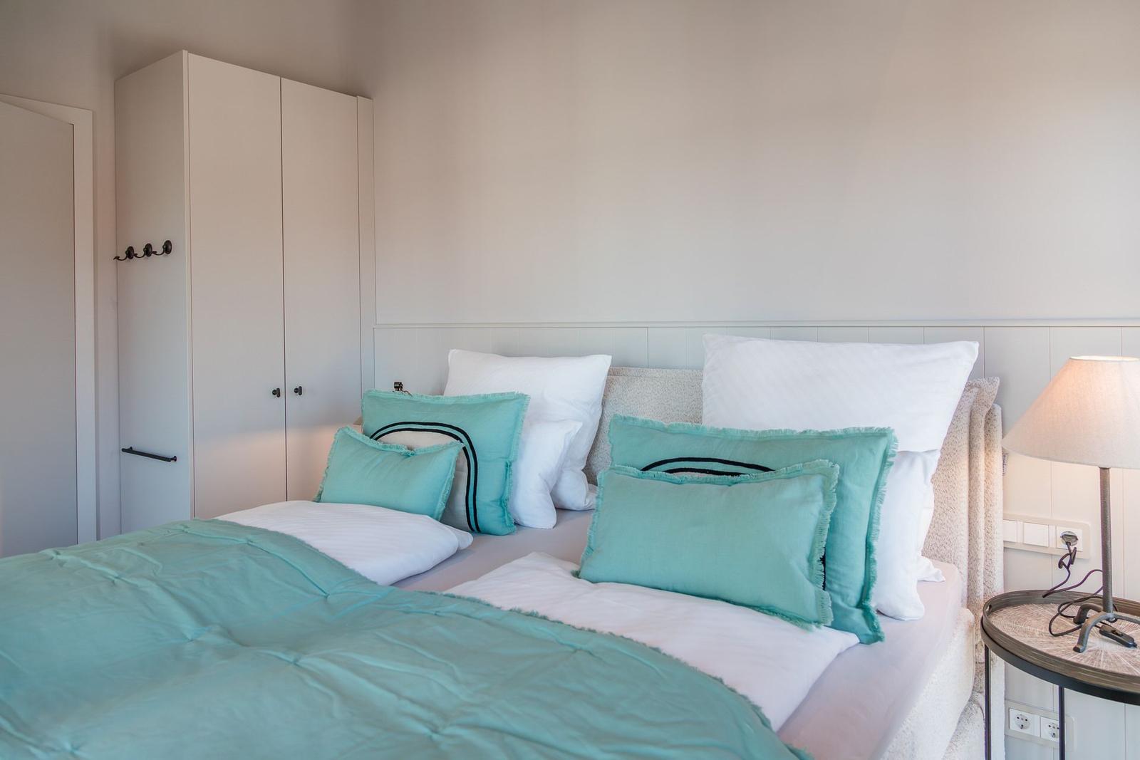 Schlafzimmer mit Bett, Kissen und Nachttisch. Hintergrund: Kleiderschrank und Wand.