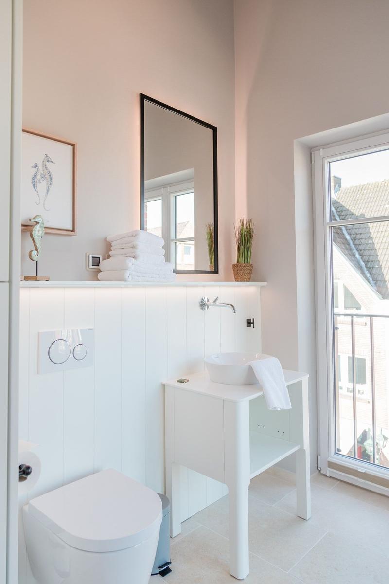 Badezimmer mit Waschtisch, Spiegel und Toilette. Fenster zeigt Balkon.
