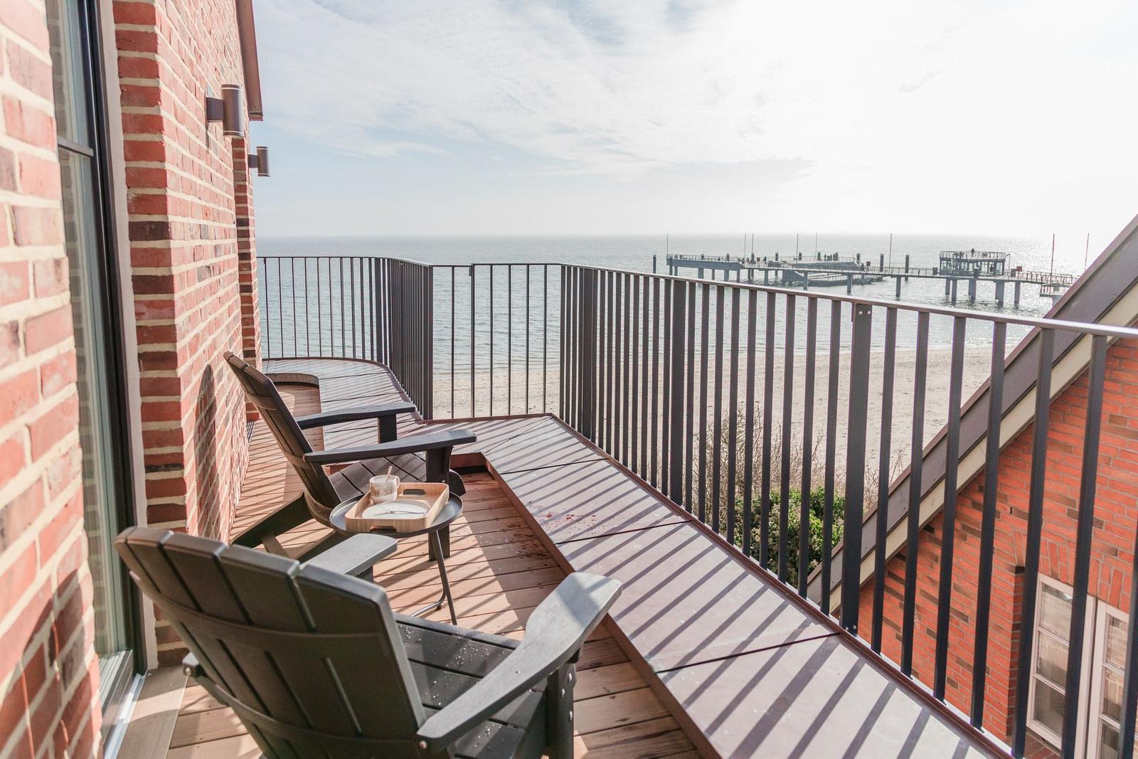 Terrasse mit Sitzgelegenheiten und Meerblick auf Pier und Strand