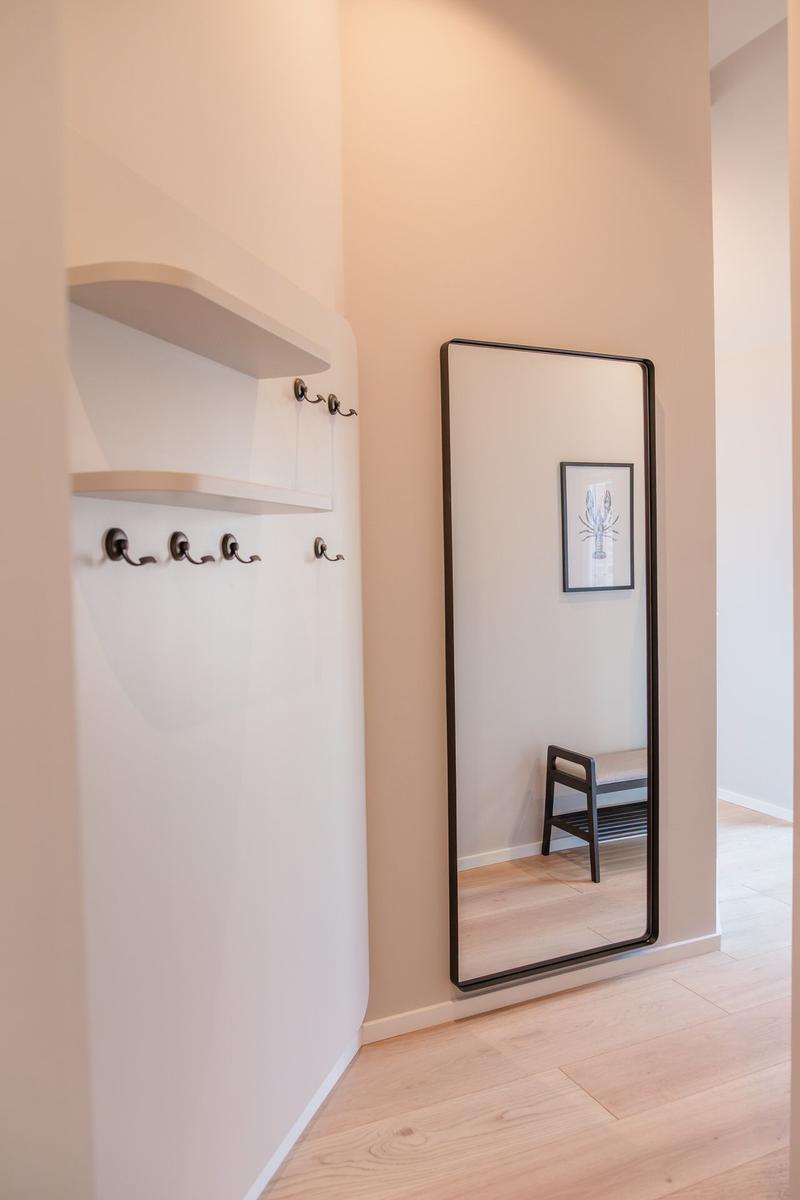 Höhenverstellbarer Spiegel mit Bild an der Wand, Kleiderhaken und Ablagefläche.