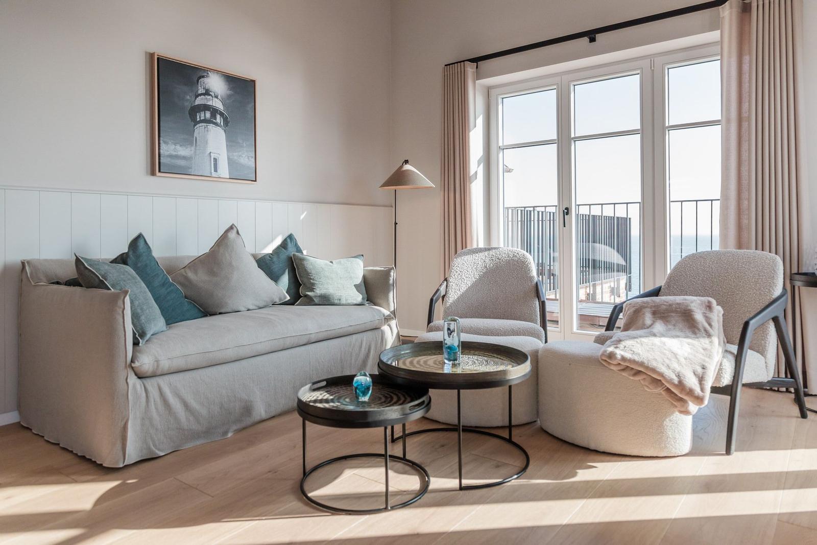 Wohnzimmer mit Sofa, zwei Sesseln und Blick auf Balkon mit Meerblick.