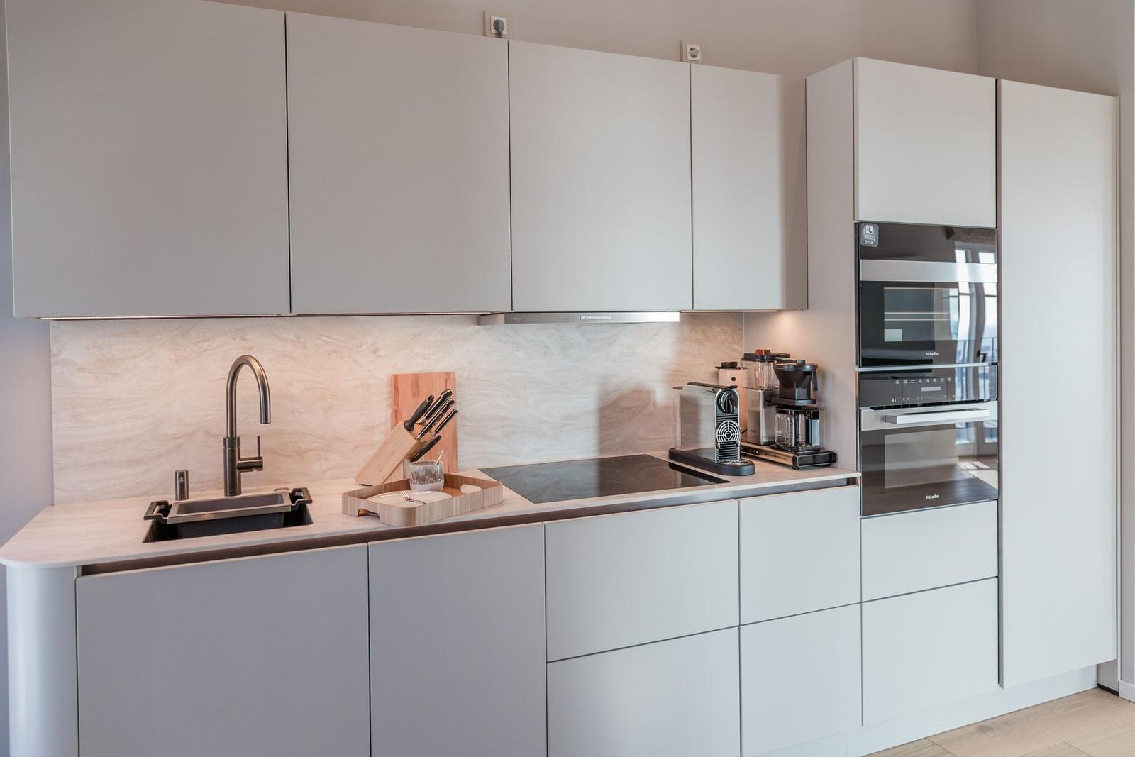Moderne Küche mit weißen Schränken, Edelstahlspüle und eingebauten Geräten.
