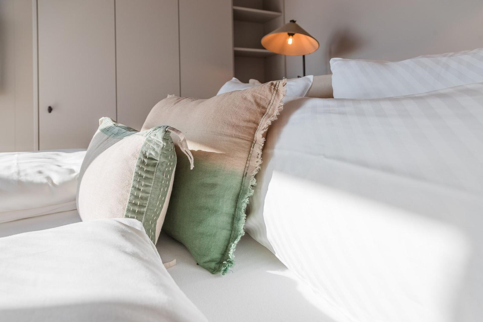 Ein Bett mit weißen Laken und mehreren Kissen in verschiedenen Farben.