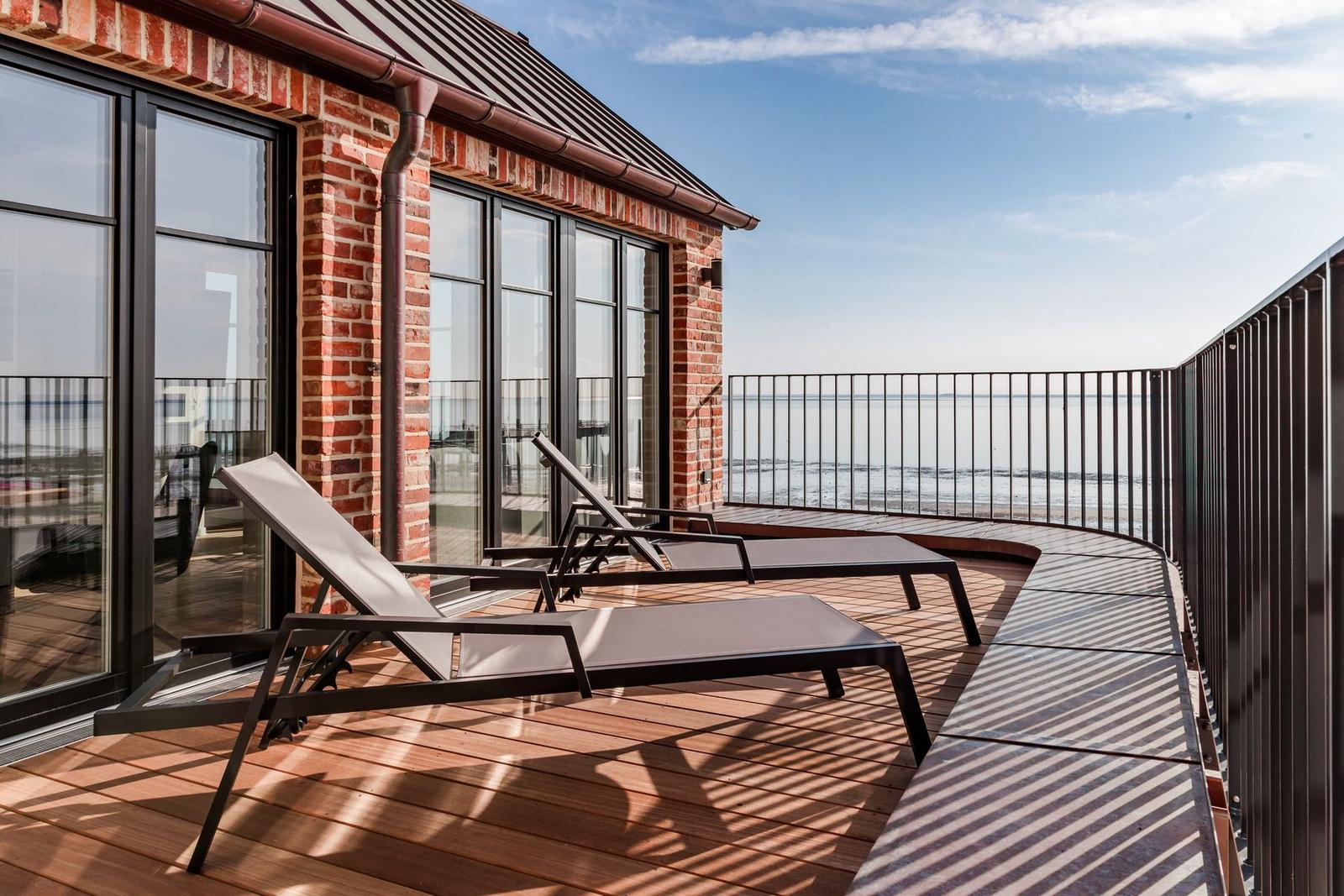 Terrasse mit Liegestühlen und Meerblick. Holzboden und Metallgeländer.