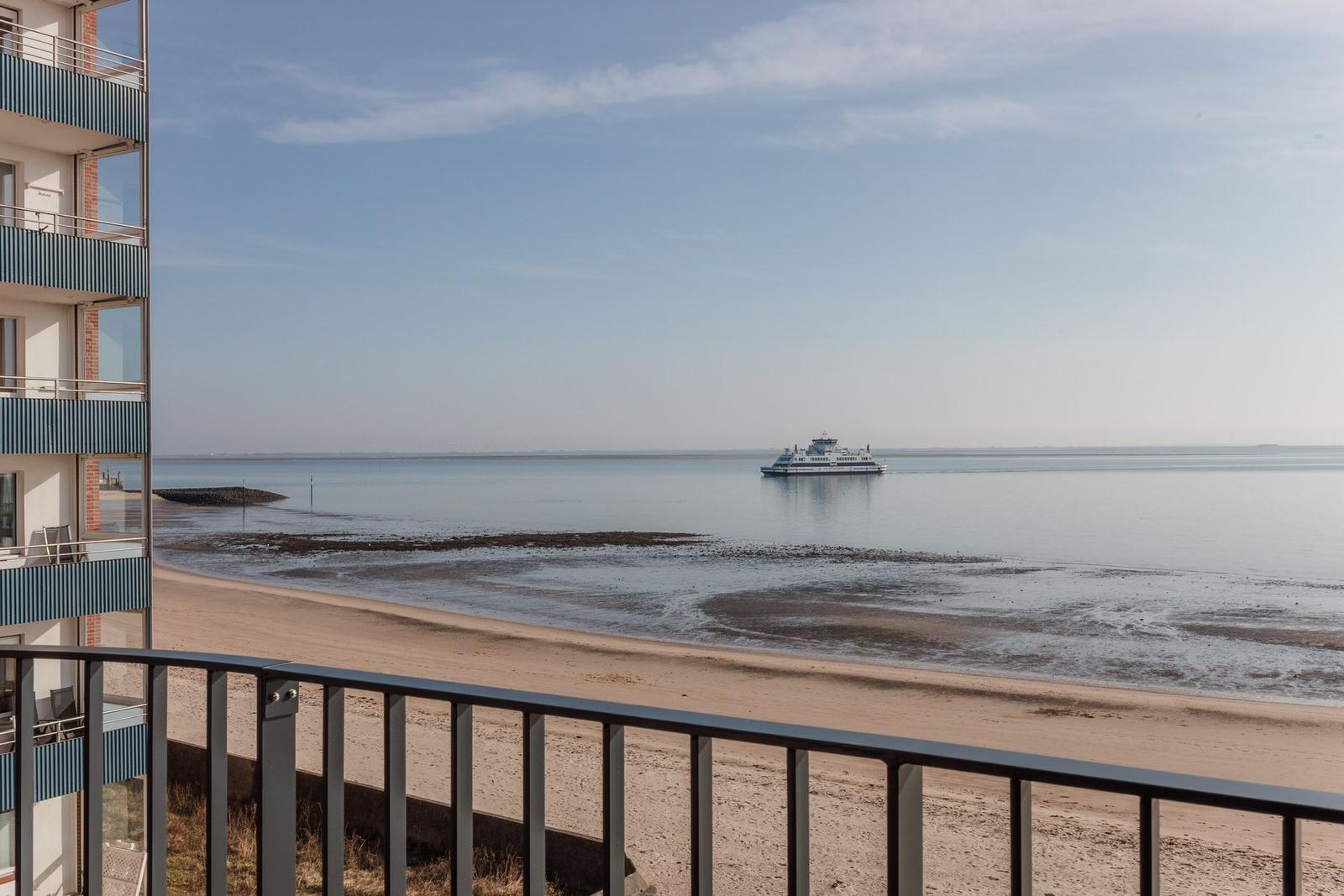 Blick vom Balkon auf Strand und Fähre im Hafen.