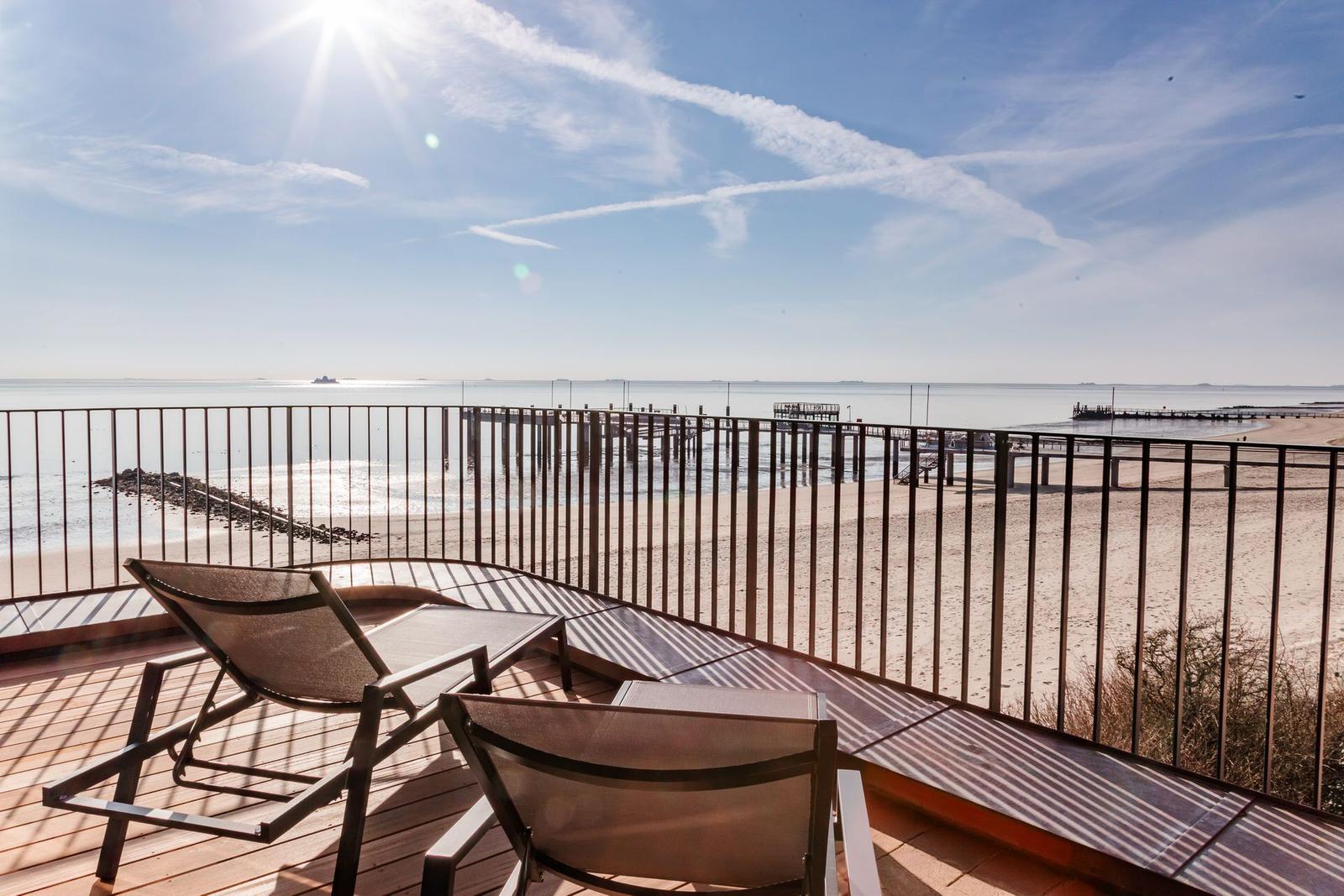 Terrasse mit Liegestühlen und Blick auf Strand und Meer.