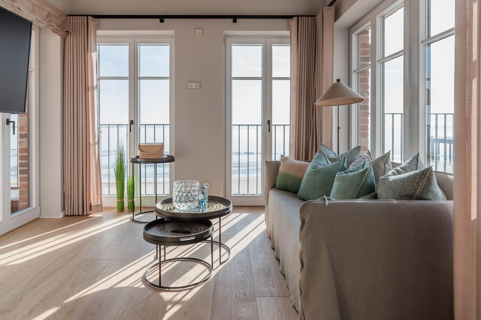 Wohnzimmer mit Sofa, Tischen und Blick aufs Meer durch große Fenster.