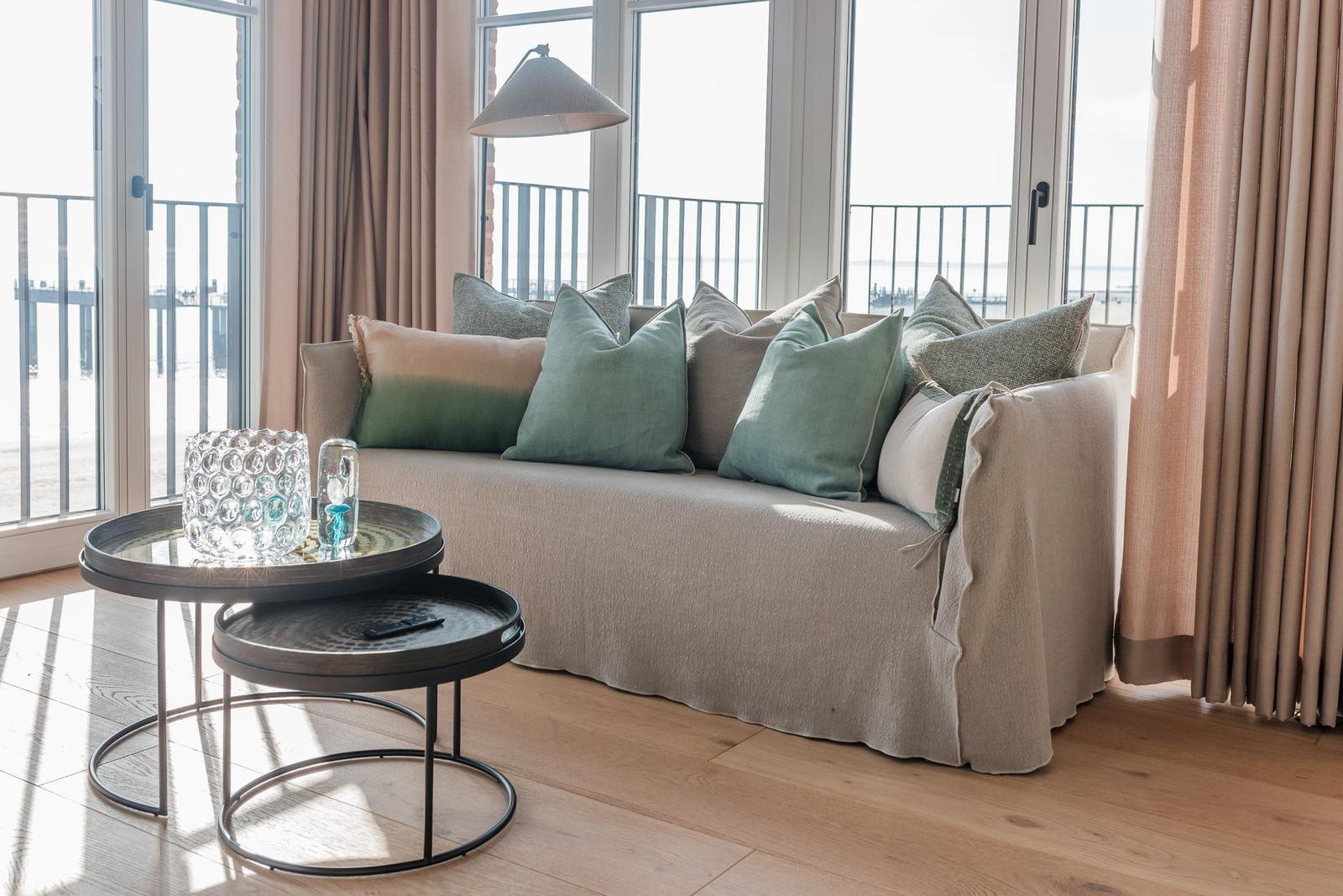 Ein Sofa mit Kissen vor großen Fenstern mit Meerblick.