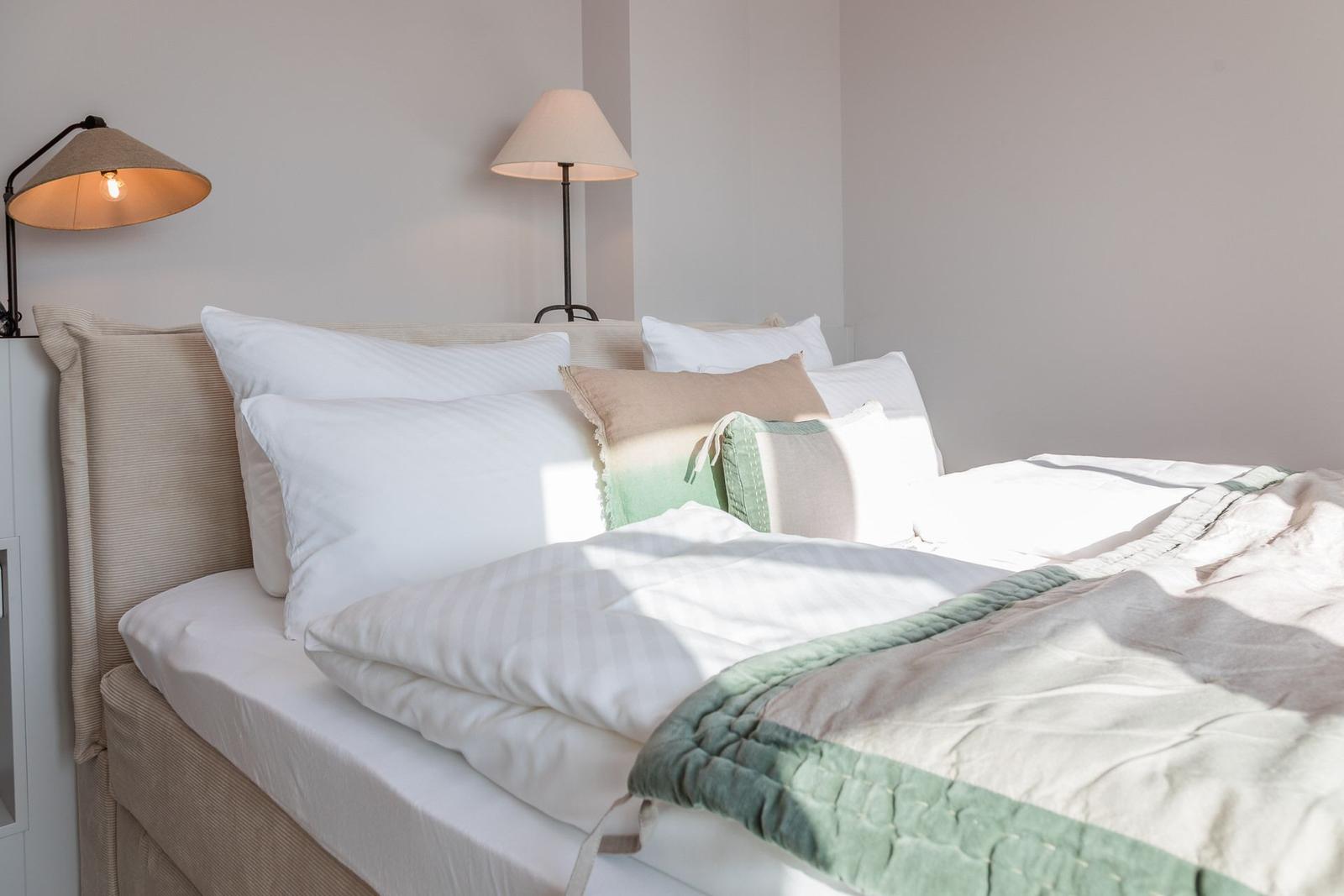 Ein Bett mit Kissen und einer Decke. Zwei Lampen stehen an der Wand.