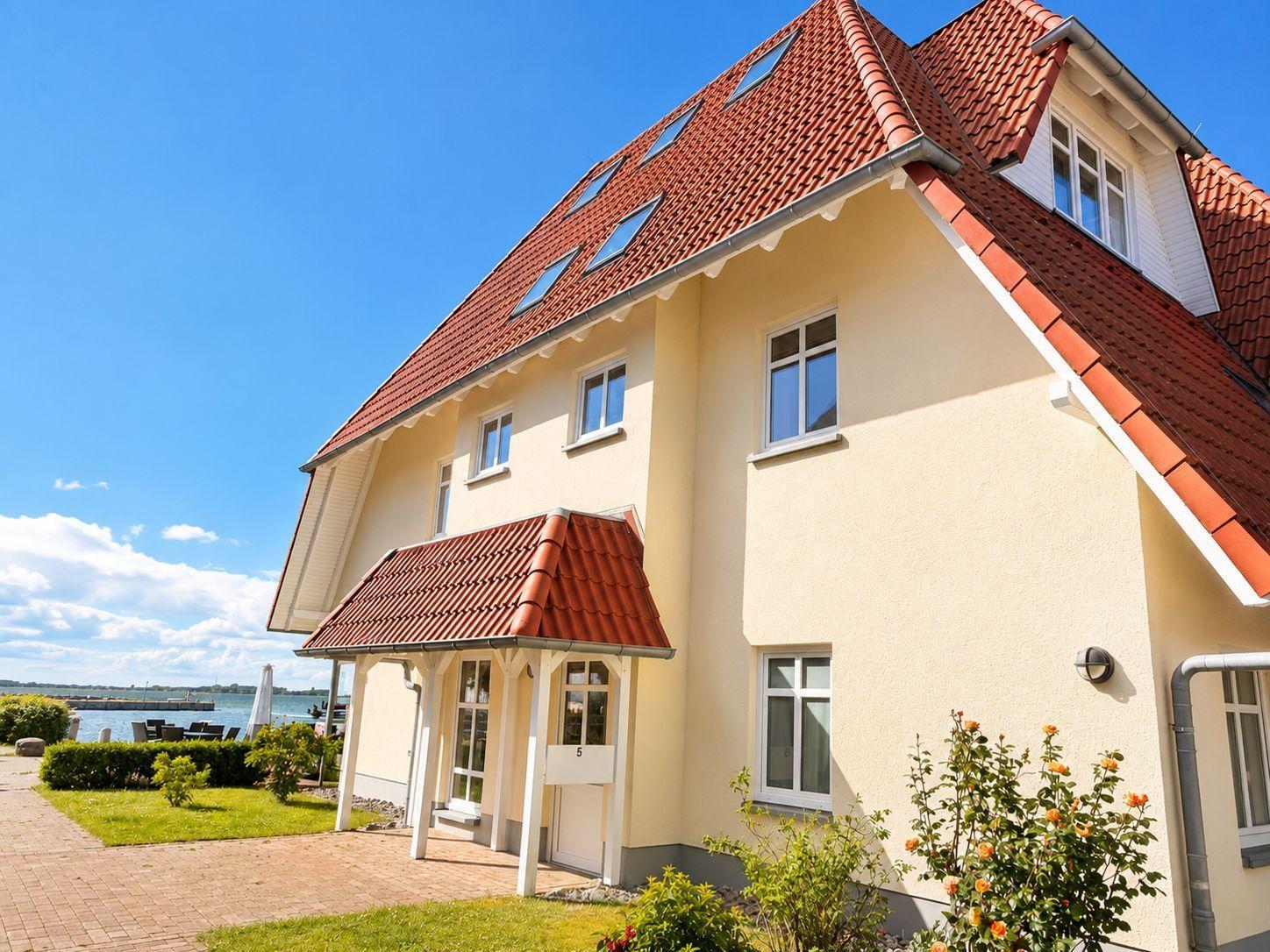 Haus mit rotem Ziegeldach und gelbem Putz, Blick auf Wasser und Himmel.