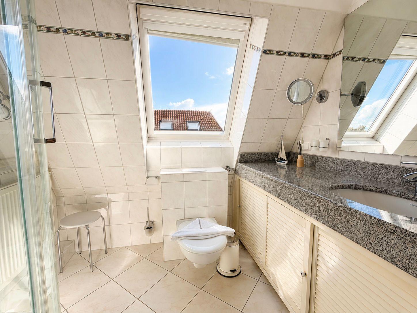Badezimmer mit Dusche, Toilette und Waschbecken unter Dachfenster.