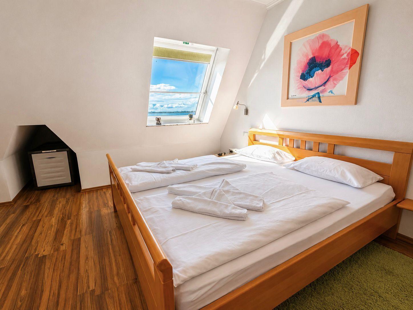 Schlafzimmer mit Dachschrägen, Holzbett, Fenster mit Meerblick und Wandbild.