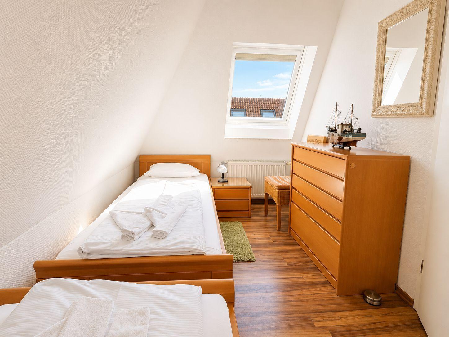Zimmer mit zwei Betten, Schrank, Nachttisch und Dachfenster mit Blick auf Dach