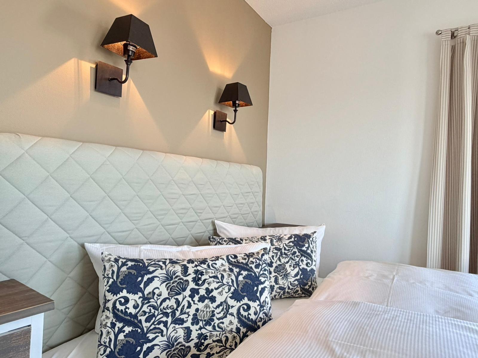 Schlafzimmer mit Bett, Kissen und Wandlampen.