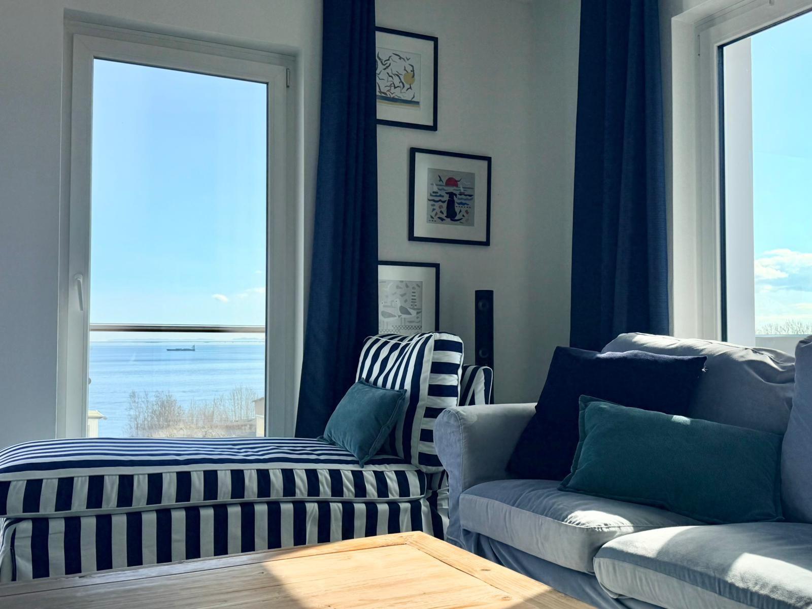 Wohnzimmer mit Sofa, Sitzbank und Blick aufs Meer durch Fenster.