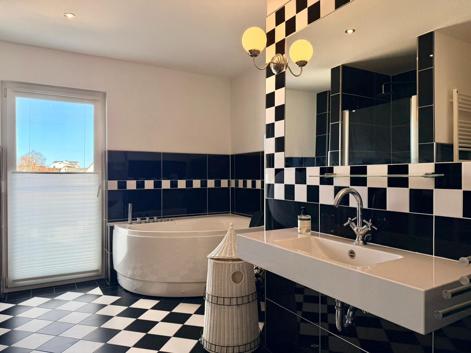 Badezimmer mit Badewanne, Waschbecken und schwarz-weißem Fliesenmuster.