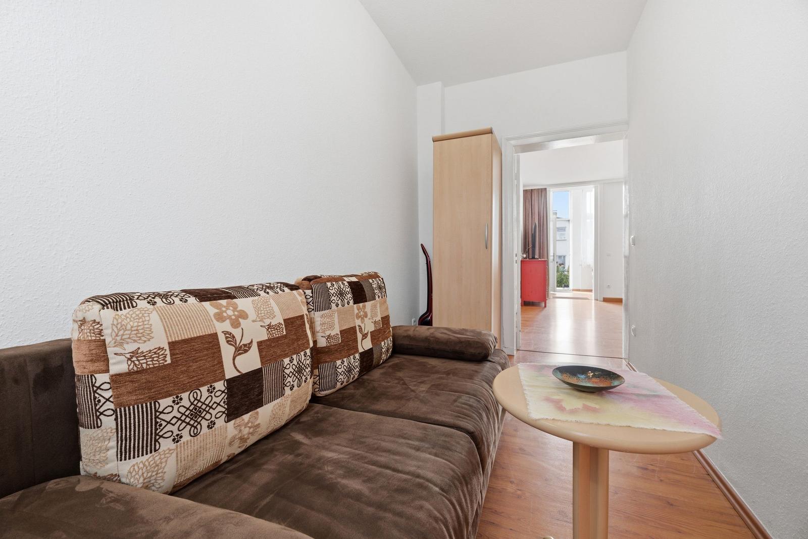 A living room with a brown sofa, patterned cushions, and a round table.