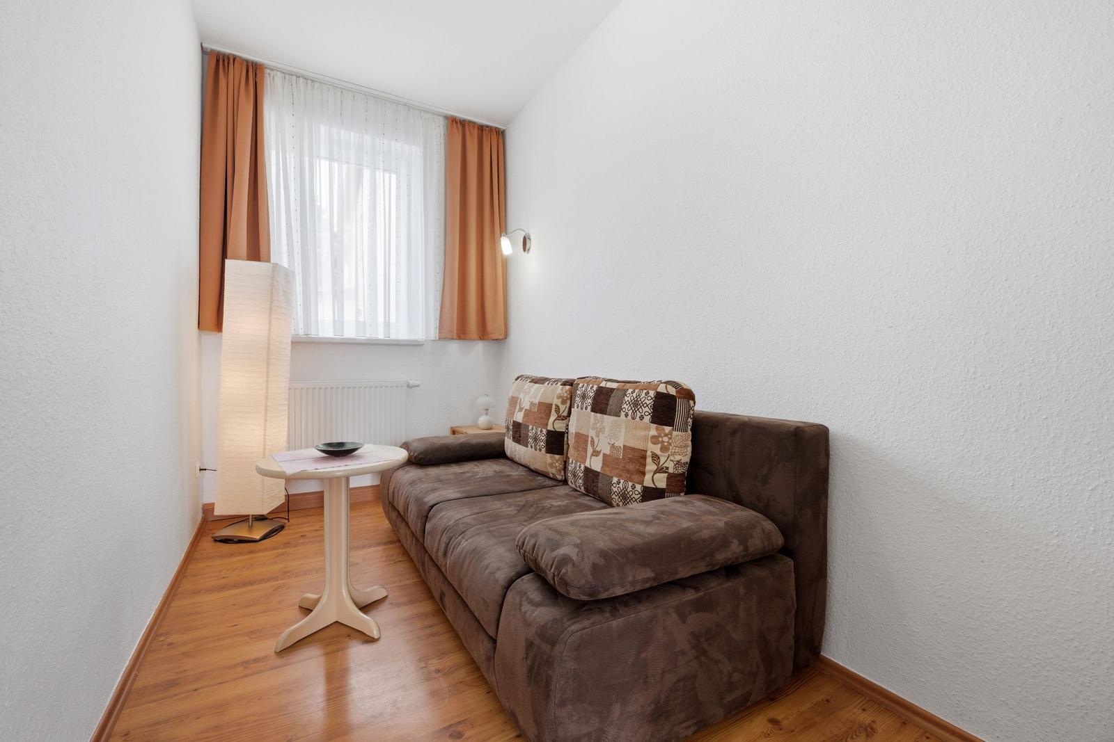 A living room with a brown sofa, wooden floor, and window with curtains.