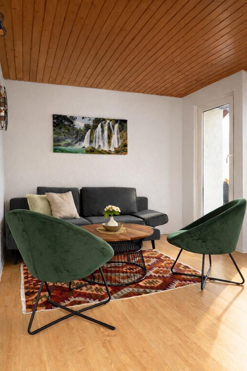 Wohnzimmer mit Sofa, zwei grünen Sesseln und Tisch auf Teppich