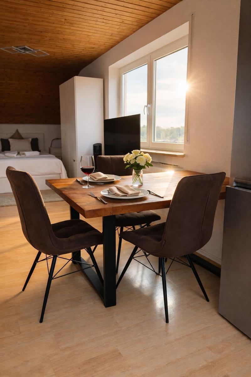 Essbereich mit Holztisch, vier Stühlen und Fensterblick. Im Hintergrund Schlafzimmer.