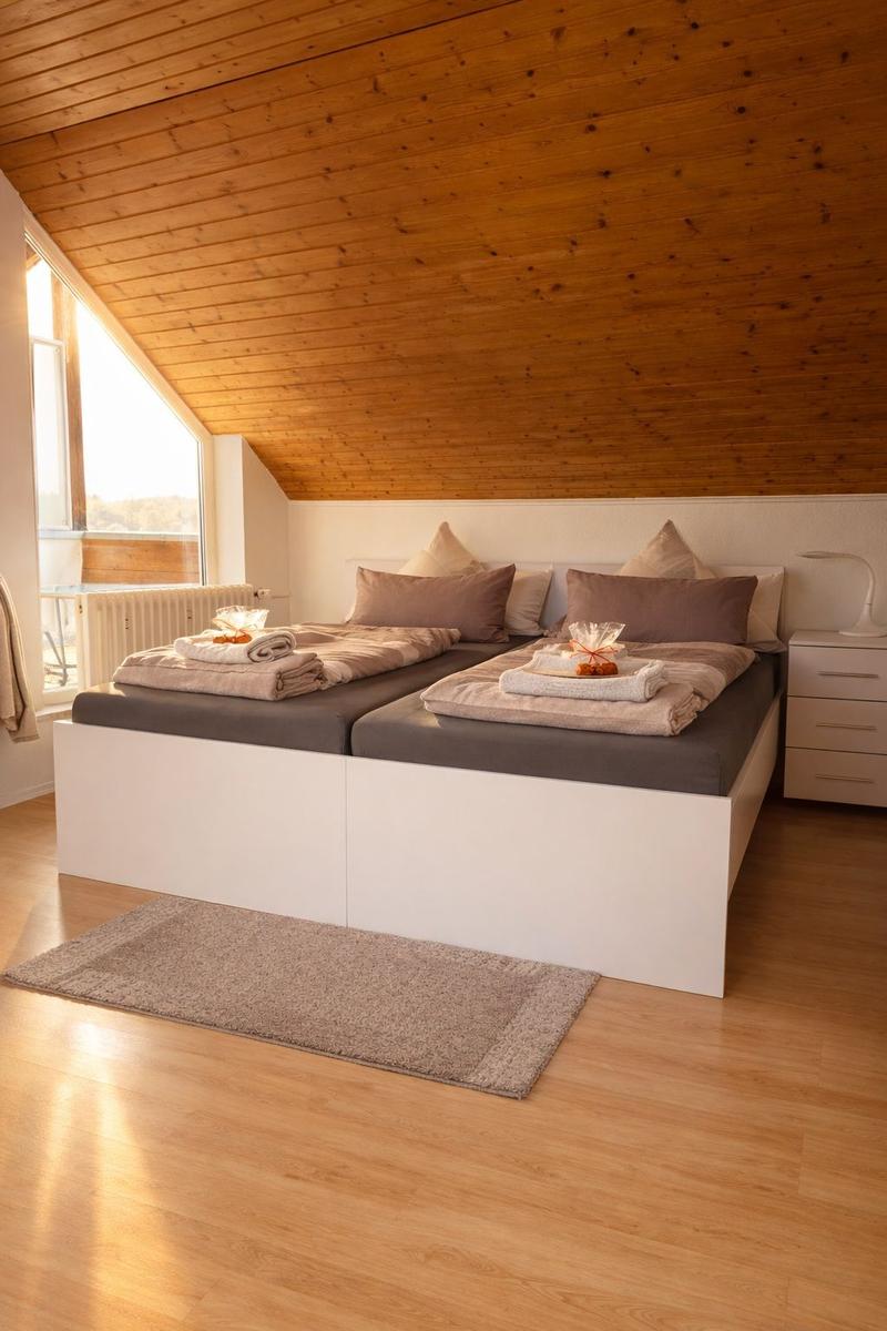 Zwei Betten mit Bettwäsche und Kissen unter einer Holzdecke. Holzfußboden und Fenster mit Blick.