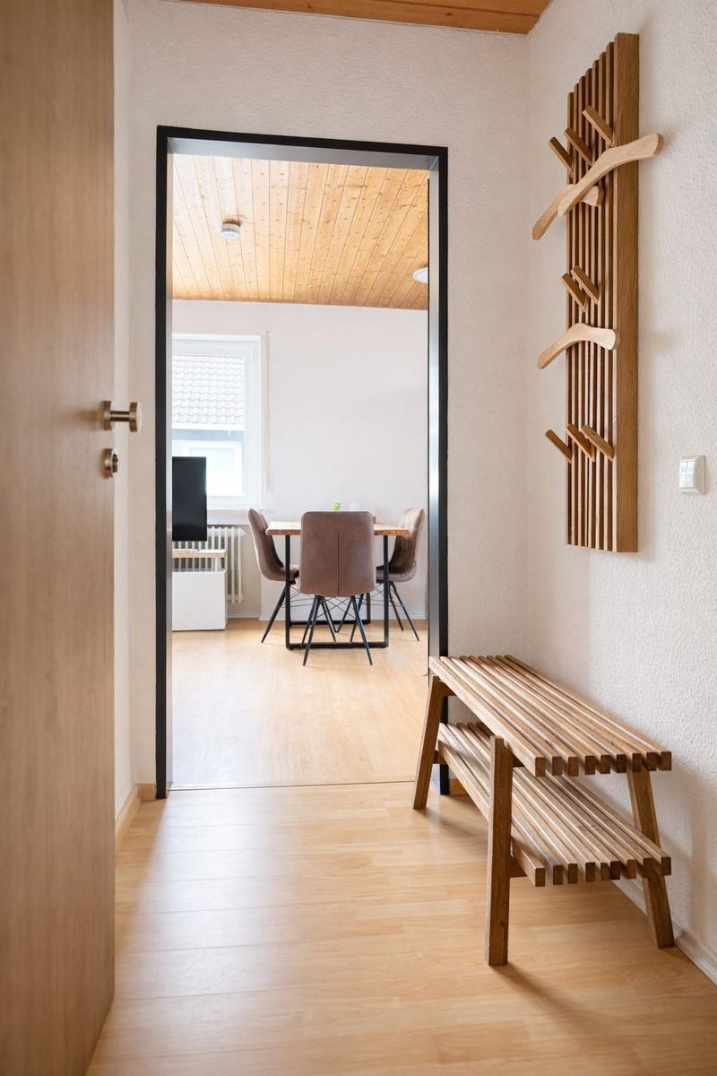 Eingangsbereich mit Holzbank und Kleiderständer. Durchgang in Esszimmer mit Tisch und Stühlen.