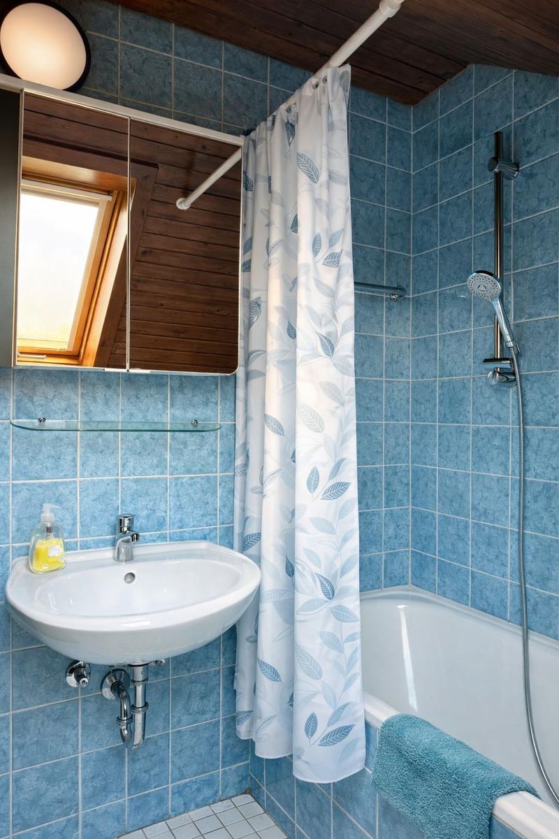 Badezimmer mit blauen Fliesen, Dusche, Waschbecken und Spiegel mit Dachfenster.