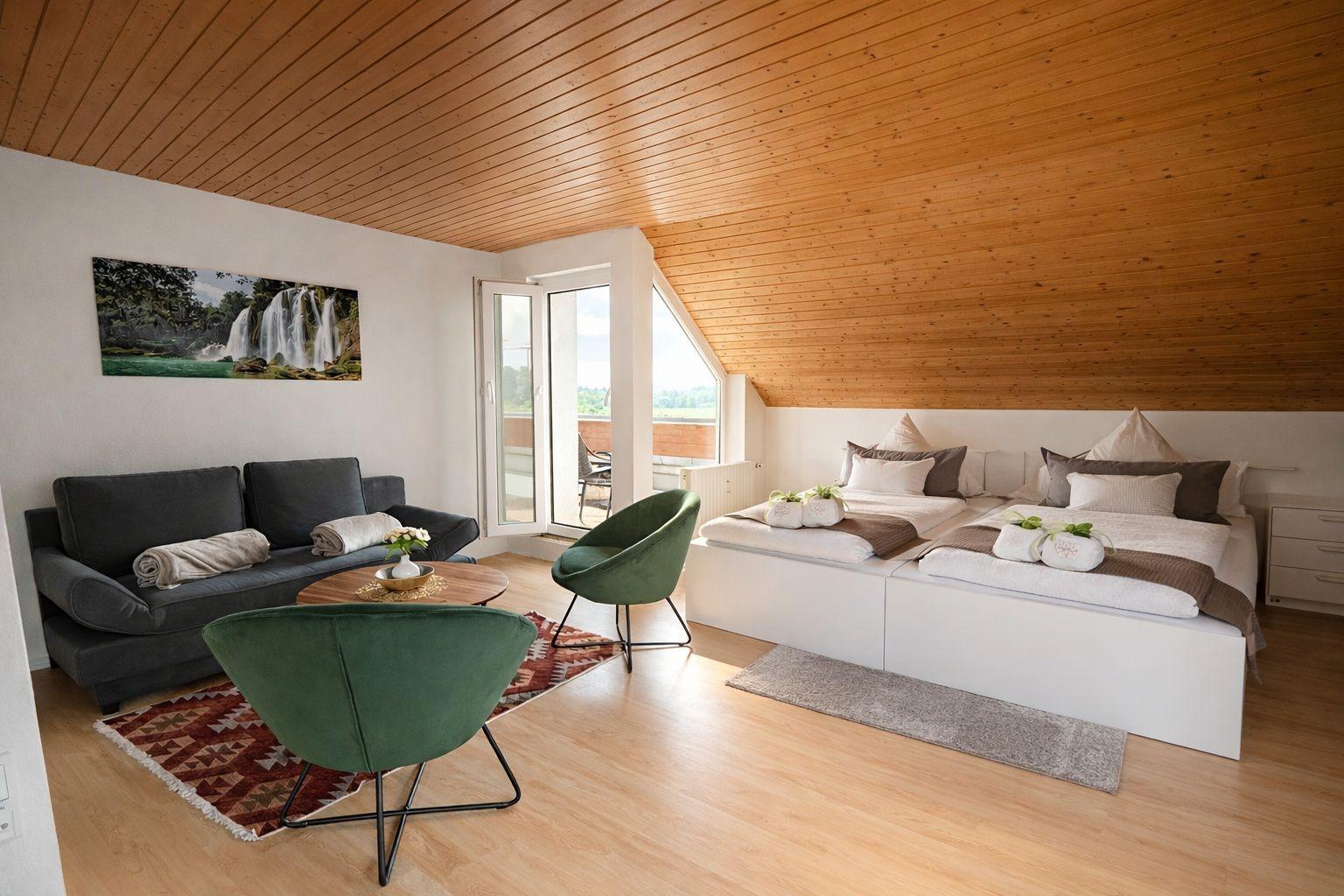 Ein Schlafzimmer mit Doppelbett, Sofa, zwei grünen Stühlen und Holzdecke.