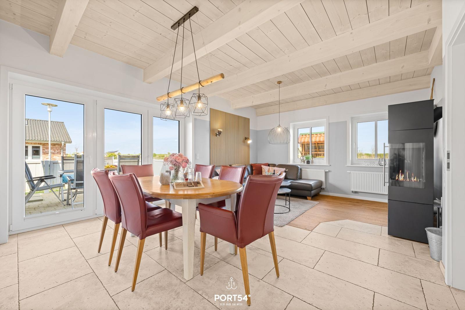 Dining area with round table and red chairs. Living area with fireplace and large windows.