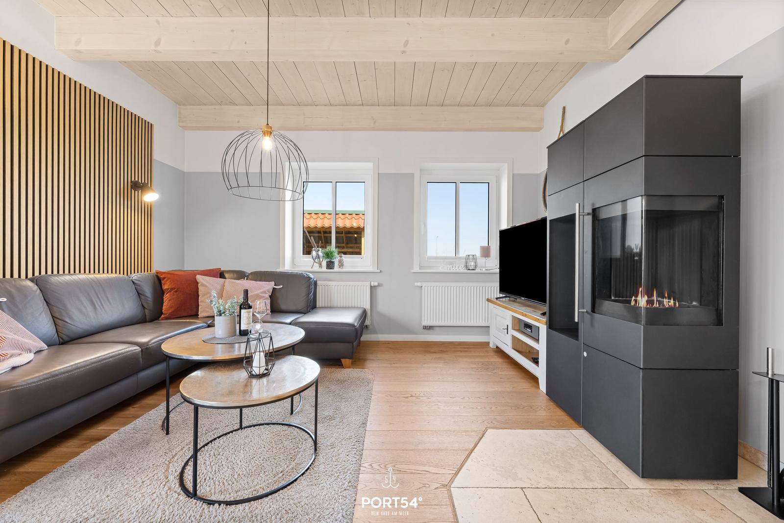 Living room with sofa, fireplace, and TV. Wooden ceiling and windows with view.