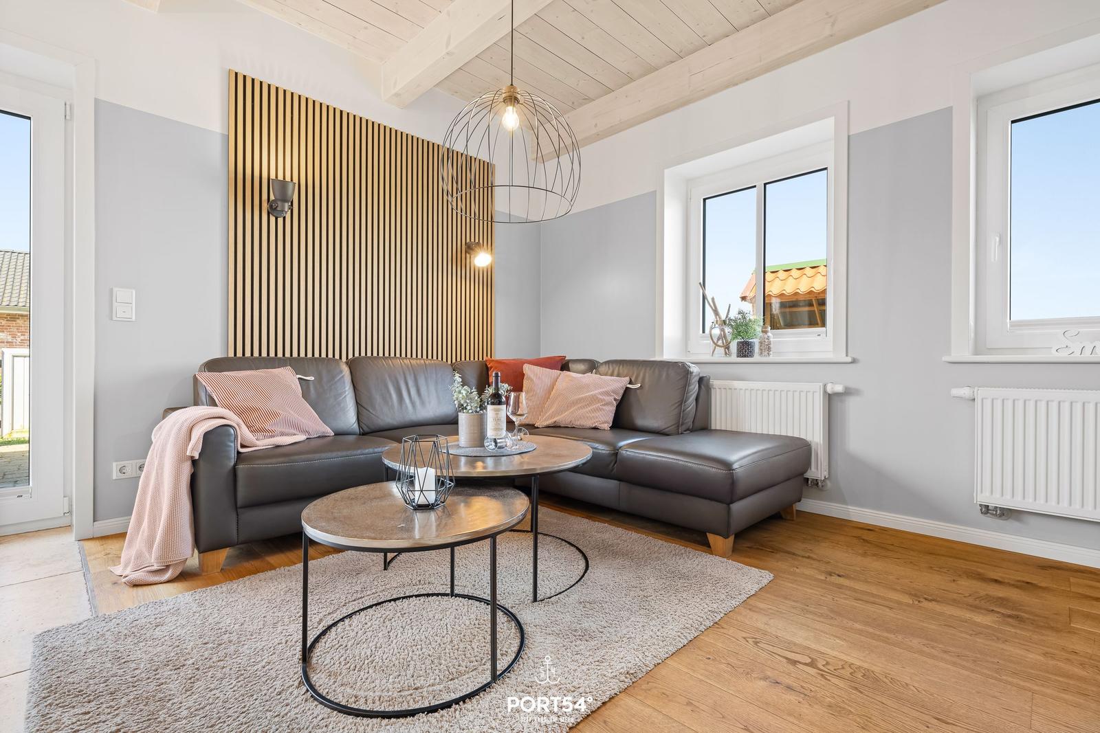 A living room with a gray sofa, wooden floor, and large windows.