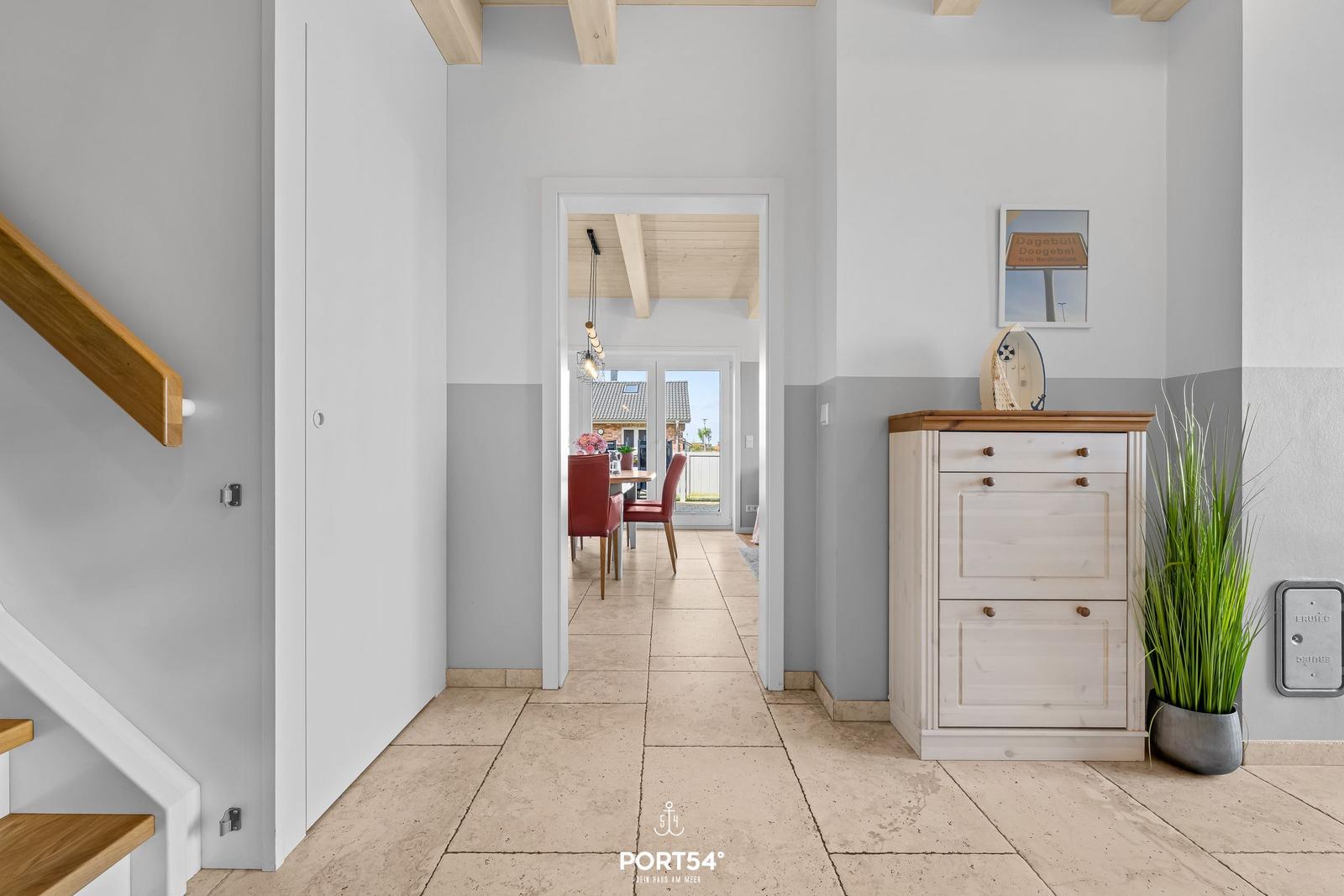 Hallway with wooden staircase, shoe cabinet, and view into dining area with red chairs.