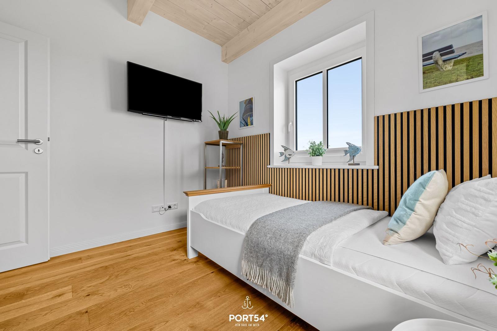 Bedroom with bed, window, TV, and wooden floor.