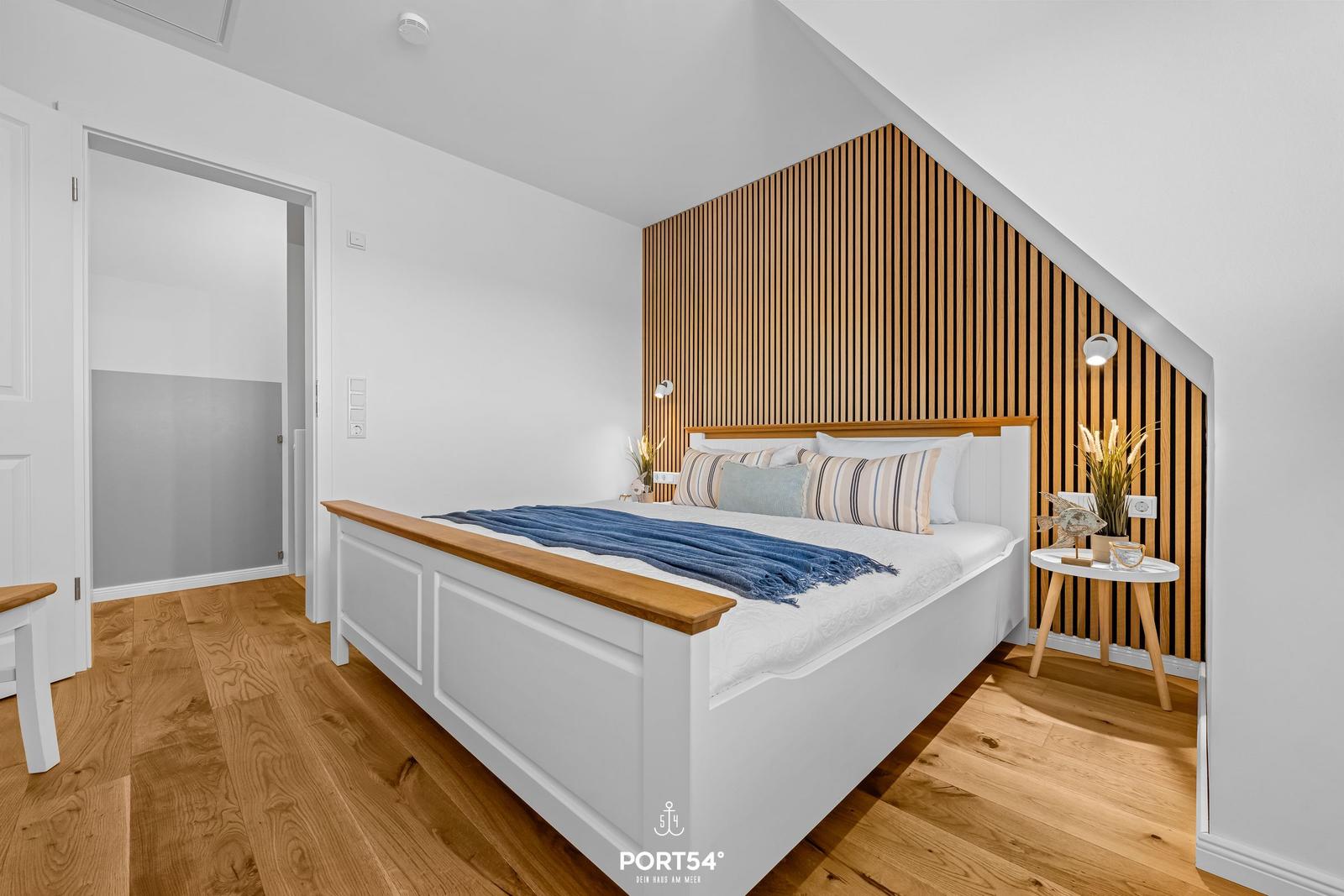 Bedroom with white bed, wooden floor, and wooden wall paneling.