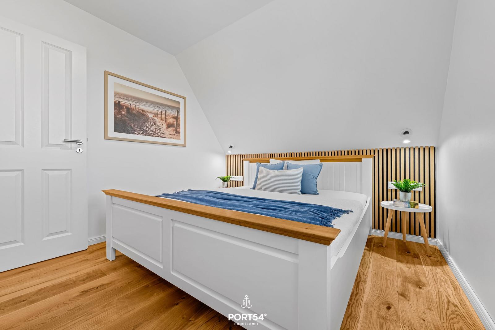 Bedroom with bed, wooden floor, and wall art. Nightstand with plant.