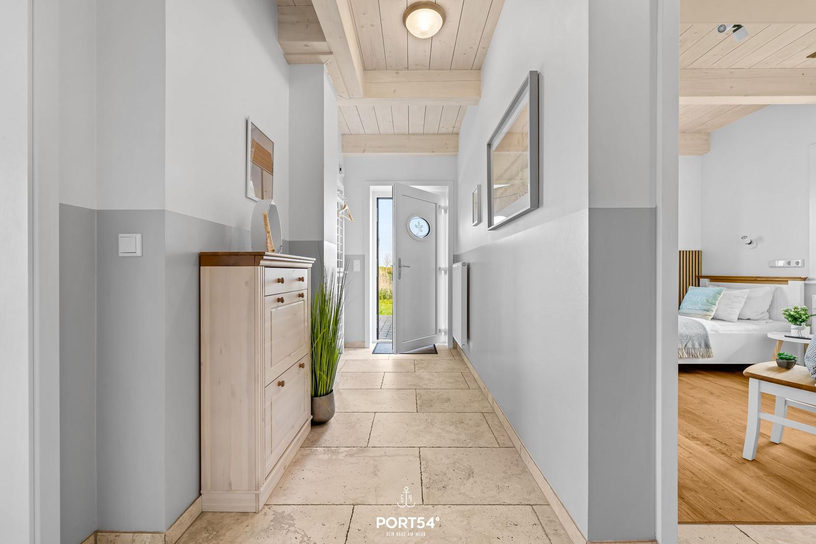 Hallway with wardrobe, plant, and view into bedroom with bed and table.