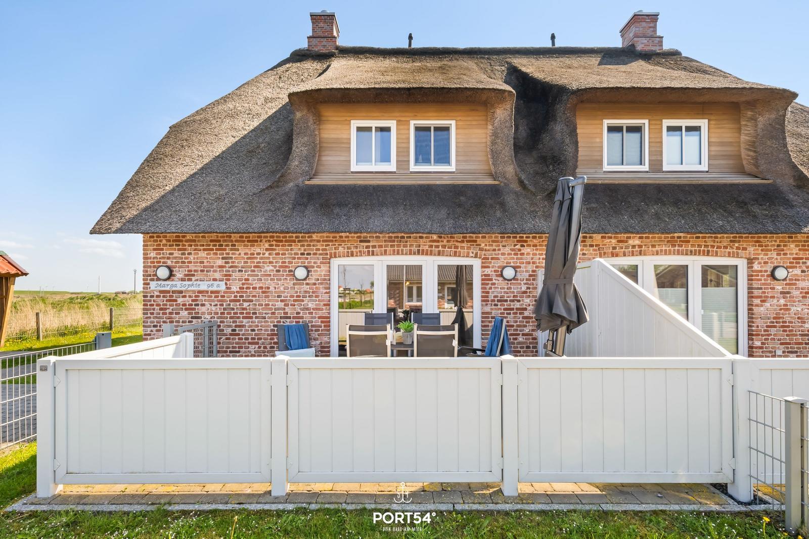 House with thatched roof, terrace, and garden fence. Windows and doors are white.