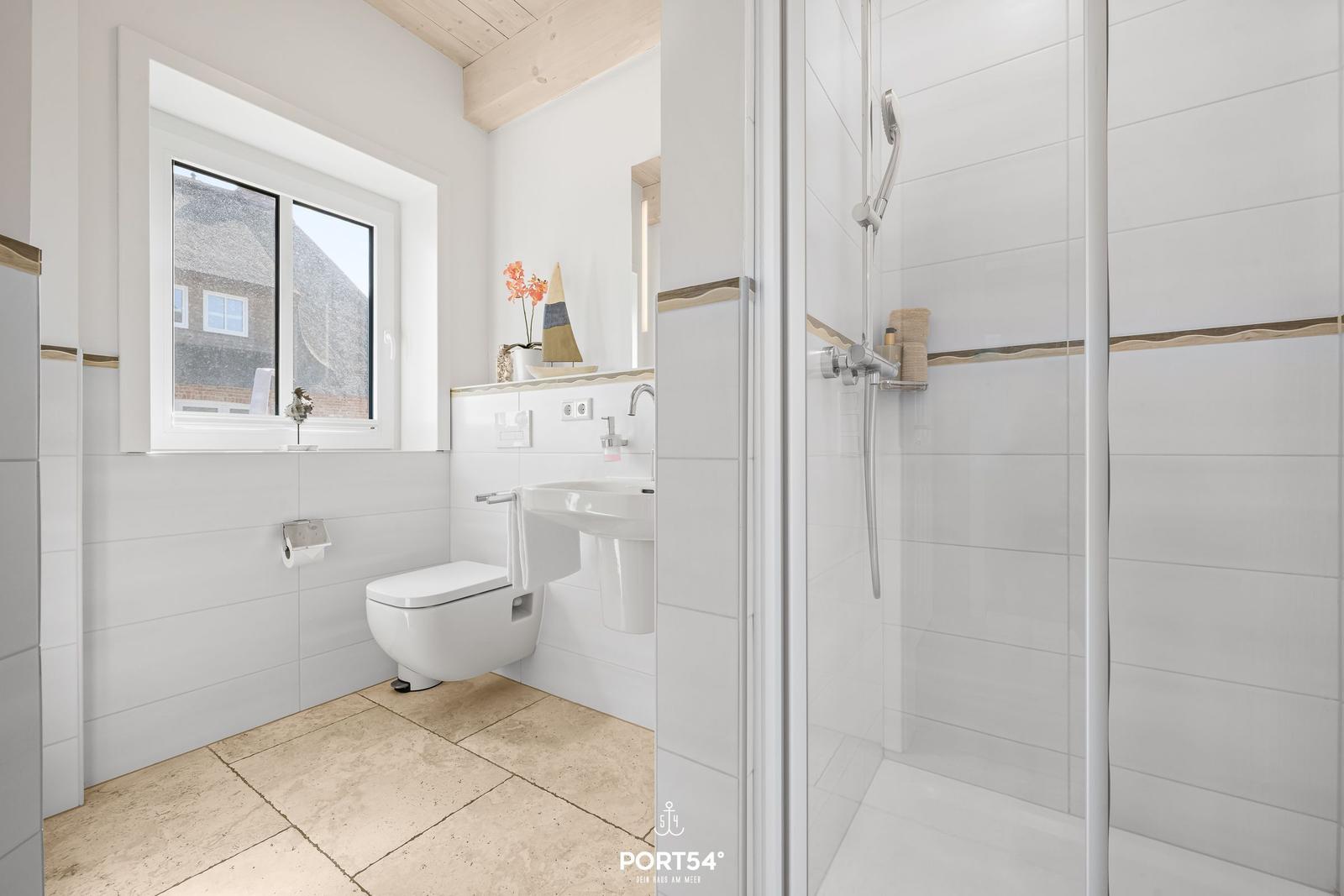 Badezimmer mit Dusche, Toilette und Waschbecken. Fenster mit Blick auf Dach.