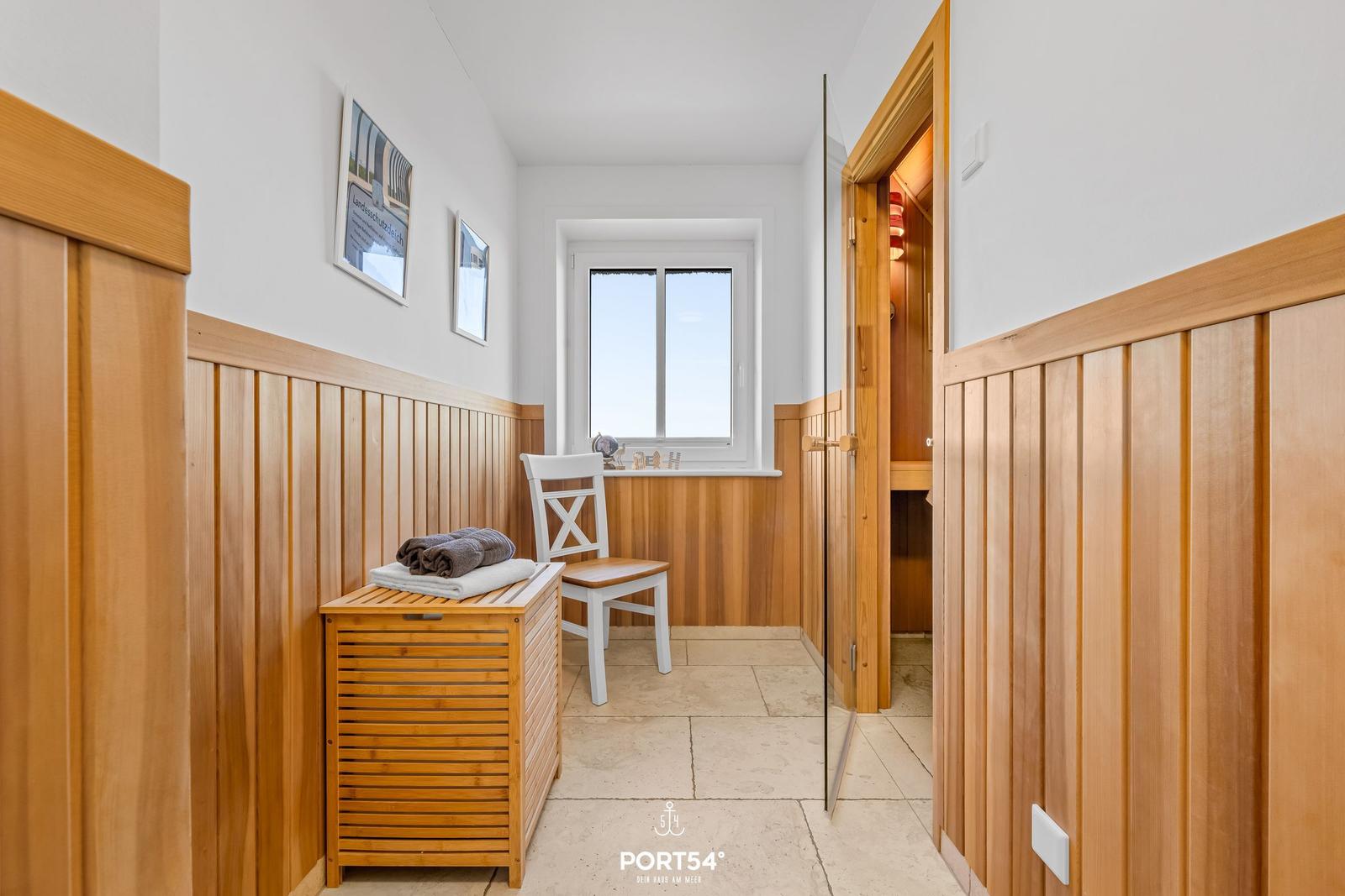 Flur mit Holzverkleidung, Stuhl und Fenster. Tür führt in die Sauna.